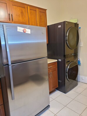 A kitchen with a stainless steel refrigerator, a washing machine, wooden cabinets, and a countertop. - Apartment near Forsyth Park with free parking. 1.3 mile walk to River Street (Savannah)