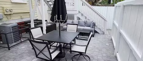Un patio exterior con mesa y sillas, una parrilla y una valla blanca.