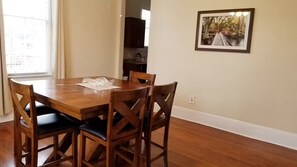 A dining area with a wooden table and chairs, a framed picture on the wall, and a view of a window. - Apartment near Forsyth Park with free parking. 1.3 mile walk to River Street (Savannah)