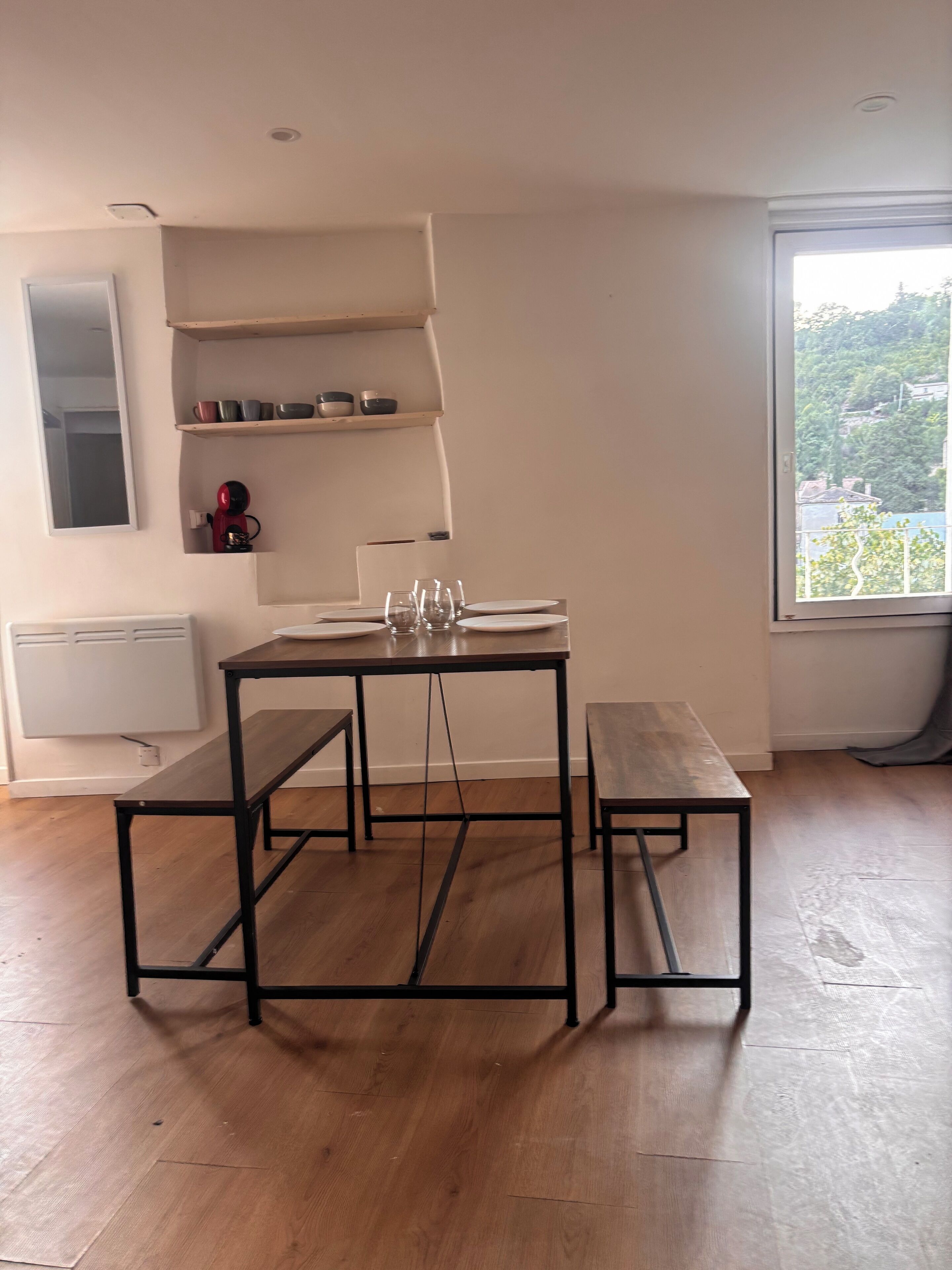 Ein Essbereich mit Tisch und Bänken, einem Heizkörper, Regalen mit Geschirr und einem Fenster mit Blick.