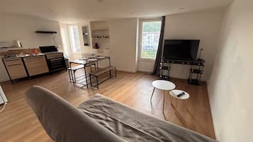 Ett modernt vardagsrum med en soffa, en matplats med bord och stolar, ett kök med spis och skåp samt en tv i hörnet.