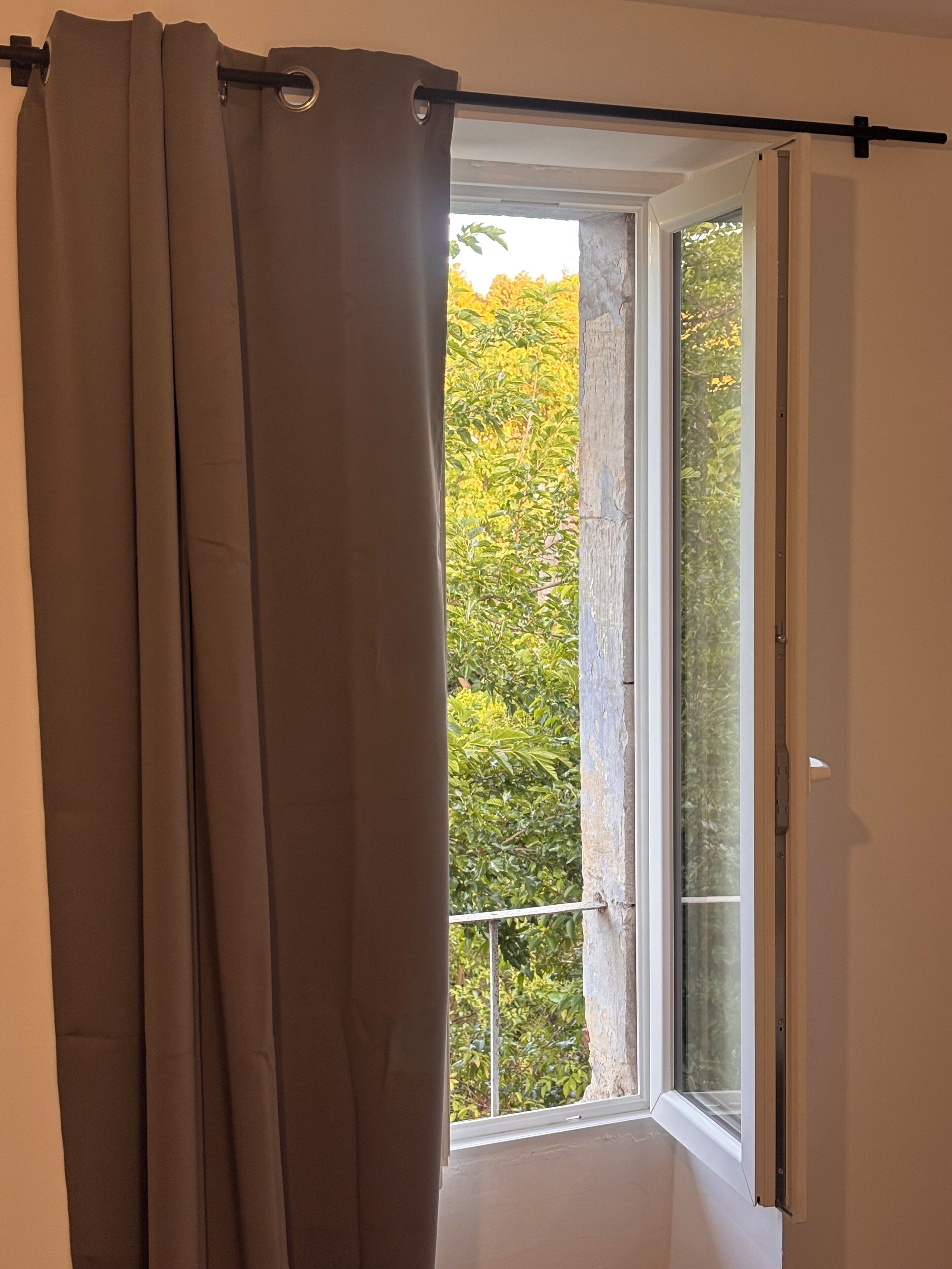 Een kamer met een raam, gordijn en uitzicht op groen.