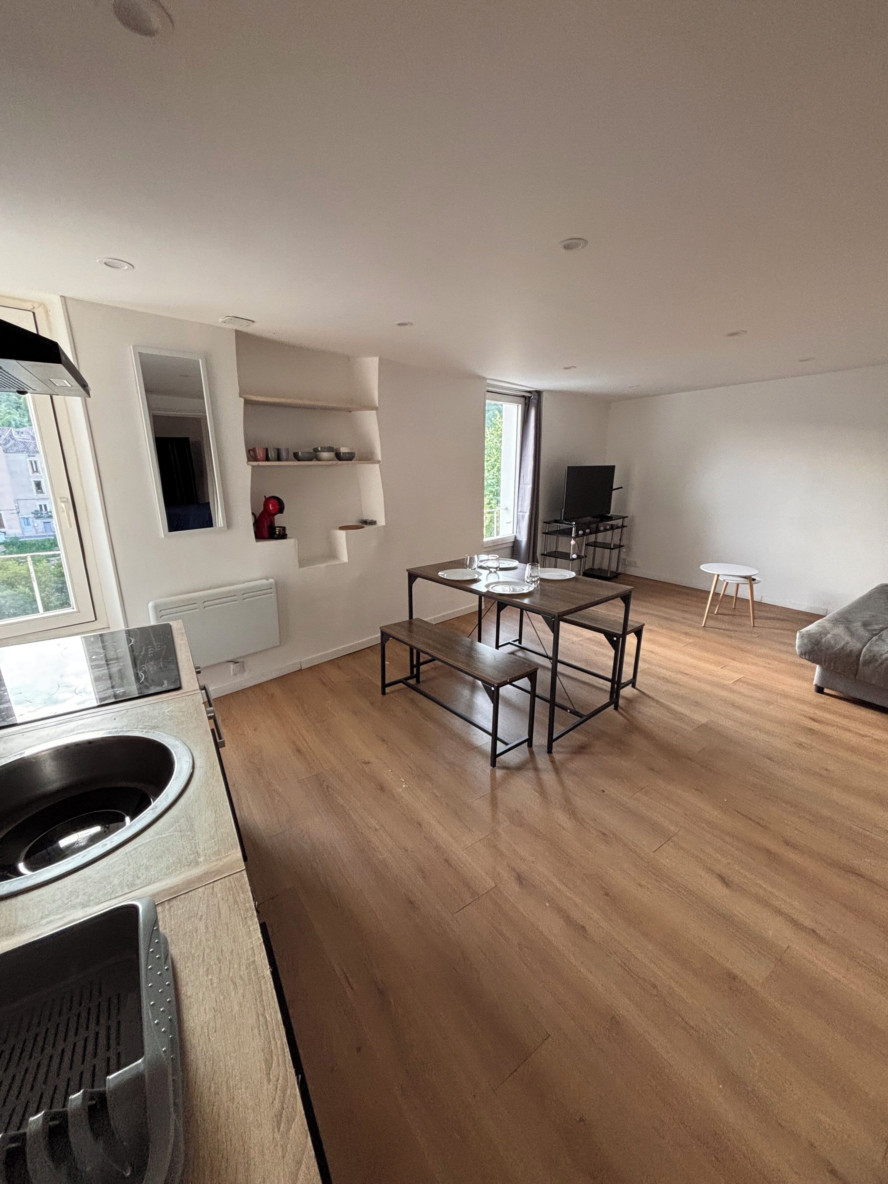 A modern kitchen with a built-in stove, wooden flooring, and a dining area with a table and benches.