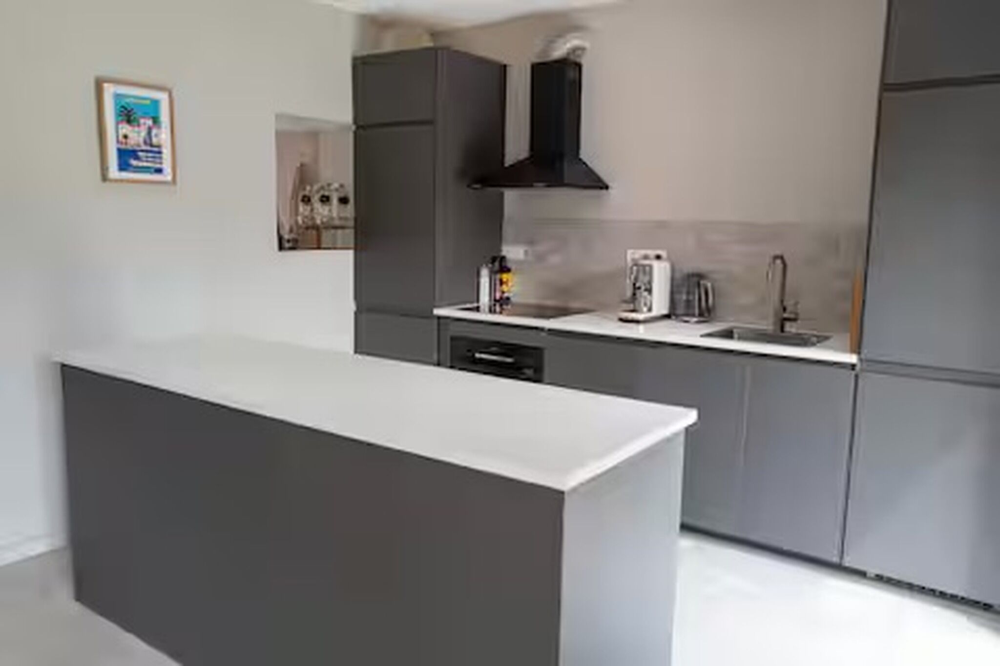 A modern kitchen with a central island, grey cabinetry, and a black range hood.