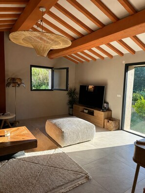 Ein modernes Wohnzimmer mit Fernseher, Holzbalken, einem großen Fenster und einer gewobenen Leuchte.