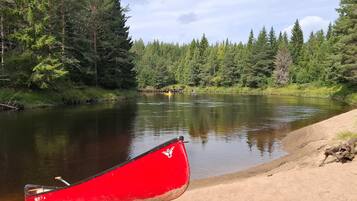En rød kano hviler på en sandet bredde ved en rolig flod, omgivet af tæt skov.