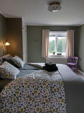 Een slaapkamer met een bed, nachtkastje, lamp, raam met gordijnen en een radiator.