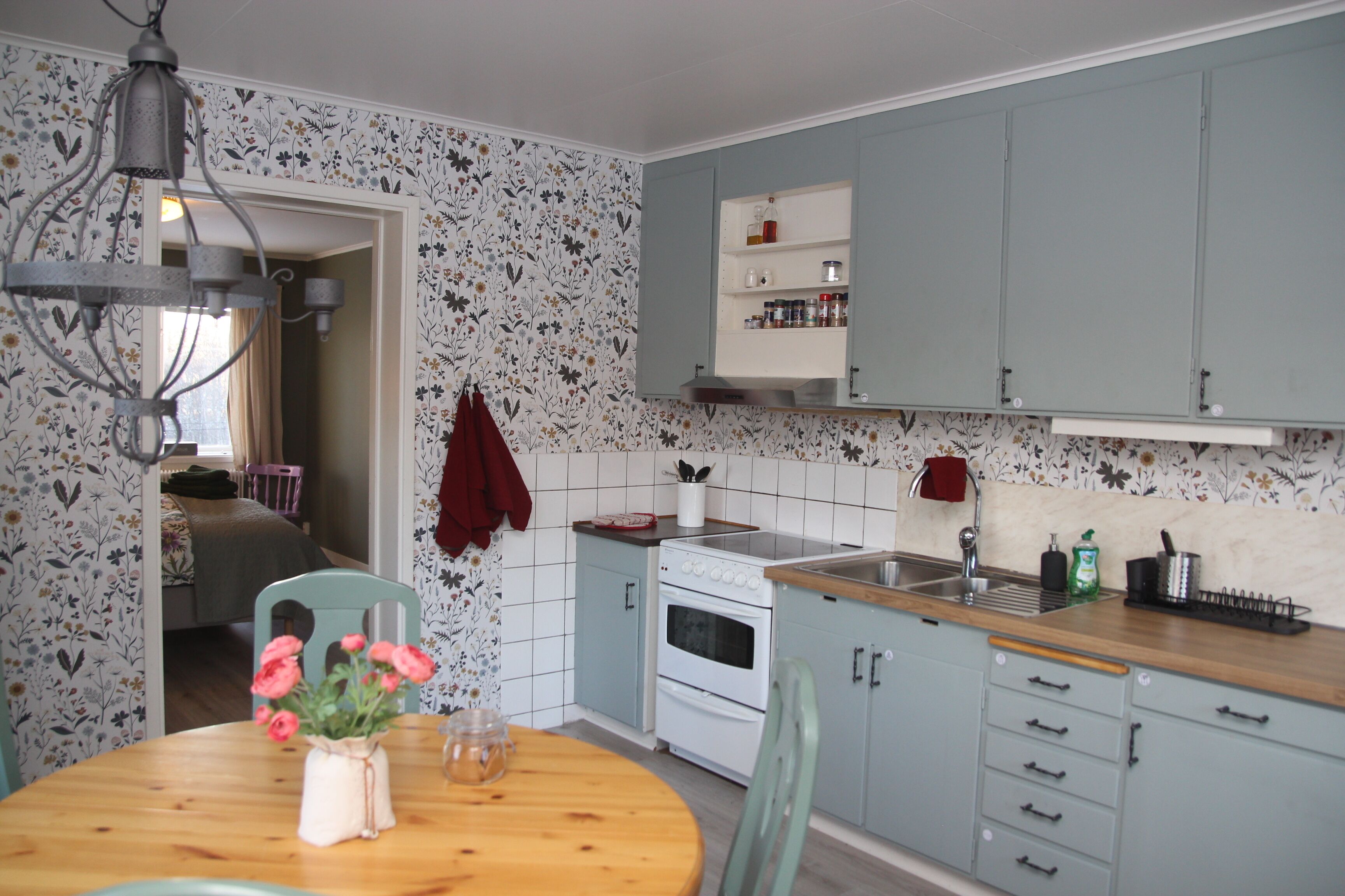A kitchen with a stove, sink, and cabinets. There is a table with a vase of flowers.