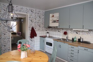 Una cocina con estufa, pileta y alacenas. Se observa una mesa con un florero.