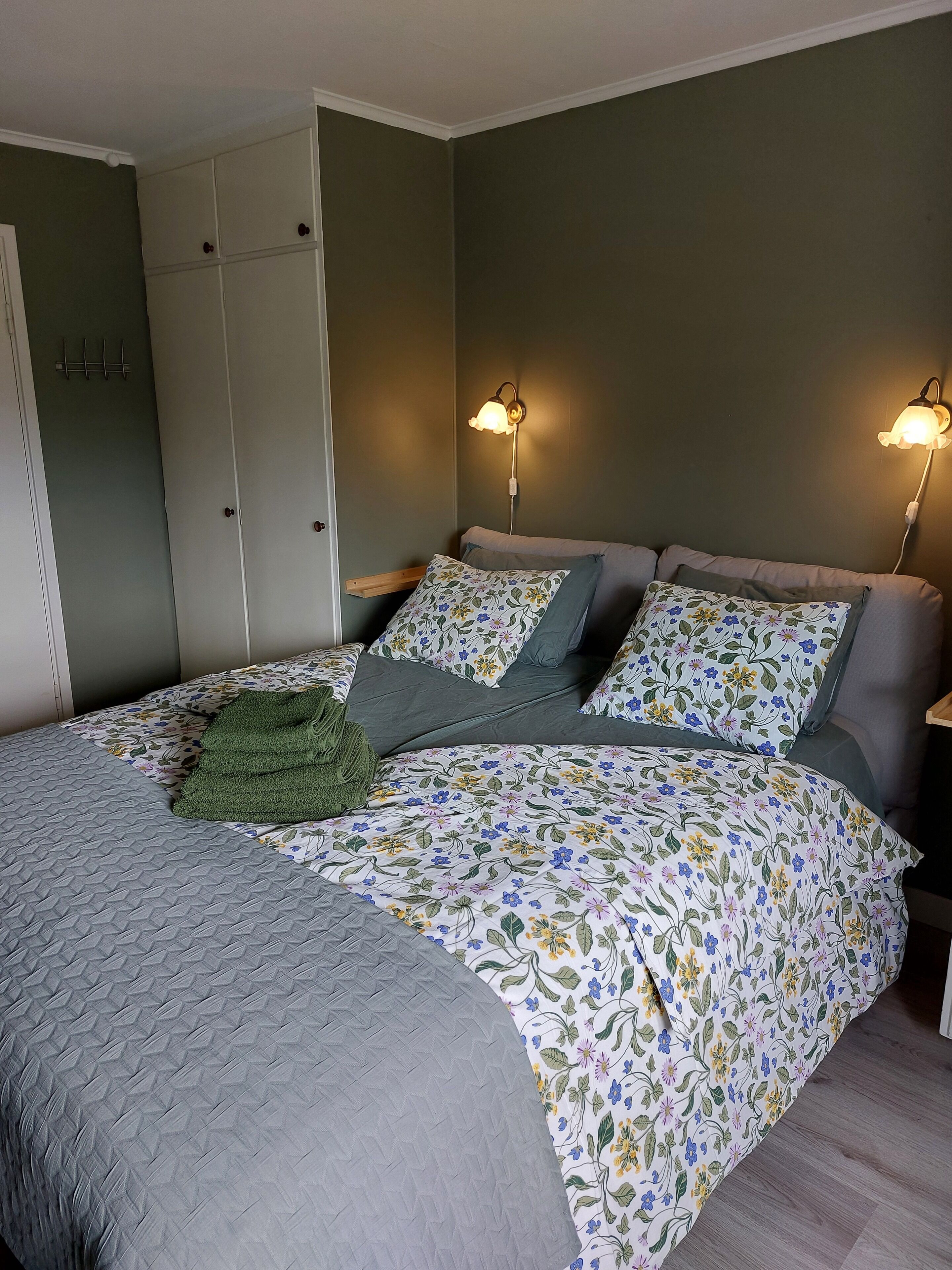 Ein Schlafzimmer mit einem Bett, zwei Nachttischlampen, einer grünen Tagesdecke und einem Kleiderschrank.