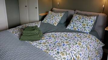 Ein Schlafzimmer mit einem Bett, zwei Nachttischlampen, einer grünen Tagesdecke und einem Kleiderschrank.