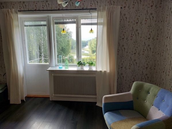 A room with a radiator, a window with curtains, a hanging lamp, and a chair.
