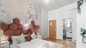 Habitación de hotel moderna con una cama grande, cabecera con diseño geométrico, mesita de noche con lámpara y vista al baño.