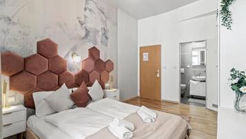 Habitación de hotel moderna con una cama grande, cabecera con diseño geométrico, mesita de noche con lámpara y vista al baño.