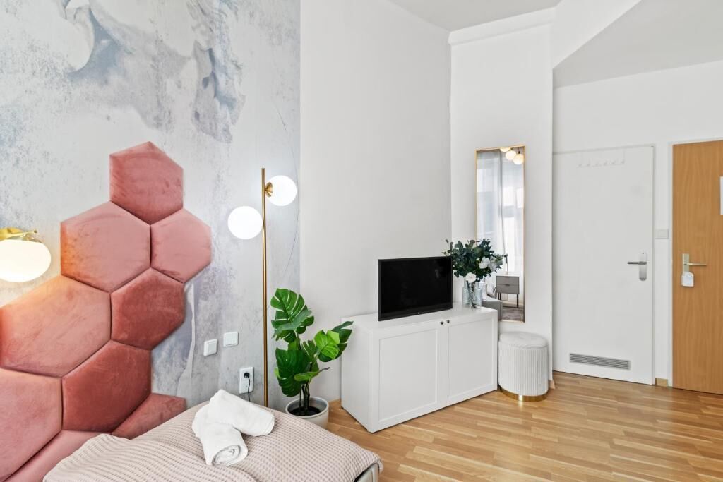 Un dormitorio moderno con una cabecera hexagonal, un televisor de pantalla plana, una planta en maceta y un armario blanco.