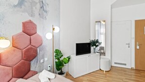 Un dormitorio moderno con una cabecera hexagonal, un televisor de pantalla plana, una planta en maceta y un armario blanco.