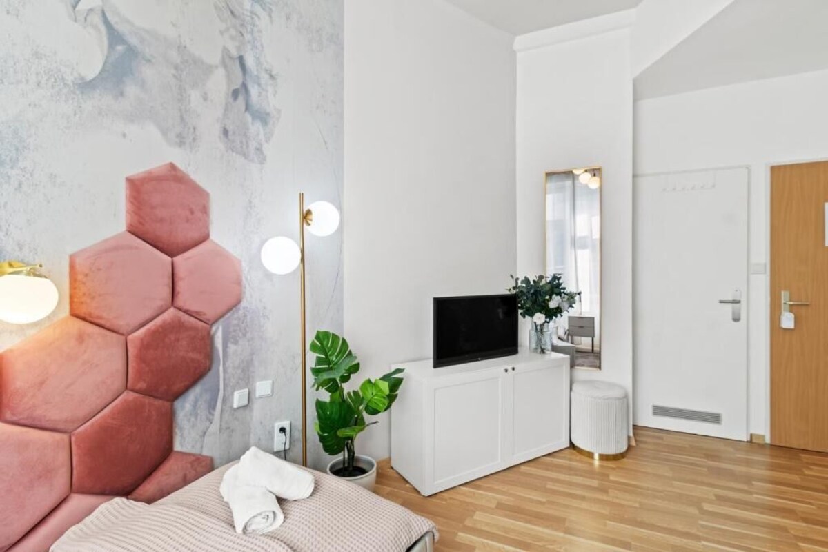 A modern bedroom with a hexagonal headboard, a flat-screen TV, a potted plant, and a white cabinet.