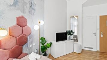 Un dormitorio moderno con una cabecera hexagonal, un televisor de pantalla plana, una planta en maceta y un armario blanco.