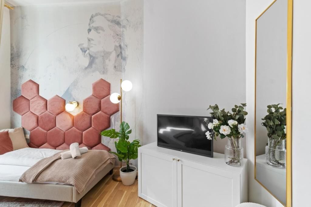 A bedroom with a bed, a TV on a cabinet, a wall with a hexagonal pattern, and a plant.