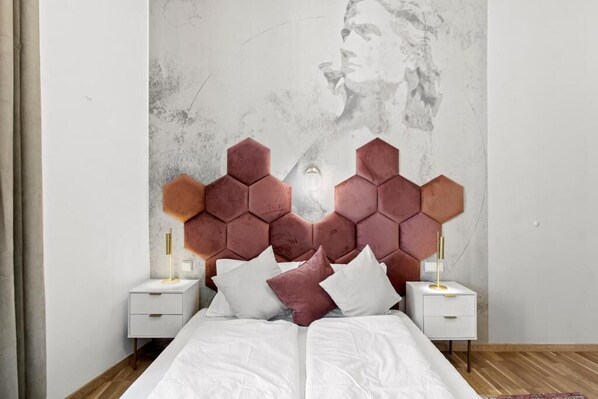 Un dormitorio con cabecera hexagonal, ropa de cama blanca y lámparas de noche.