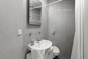 A modern bathroom with a sink, toilet, and a shower area. -  Comfort Hotel Room near Prater & City Center (Austria)