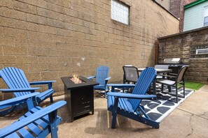 Eine Terrasse mit Adirondack-Stühlen, einem Feuerkorb und einem Grill.