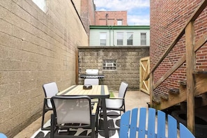 A small outdoor patio area with a table and chairs, a grill, and a brick wall. - Designer Rowhouse w/ Themed Bedrooms, Fireplace & Arcade — Perfect for Groups (Pittsburgh)