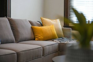A sectional sofa with multiple cushions, a small round table, and a plant in the foreground. - Sleeps 10 · Walk to Carson St · BBQ & Fire Pit (Pittsburgh)