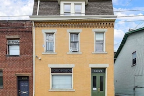 A two-story building with a green door labeled '1319' and a window with a closed shutter. - Designer Rowhouse w/ Themed Bedrooms, Fireplace & Arcade — Perfect for Groups (Pittsburgh)