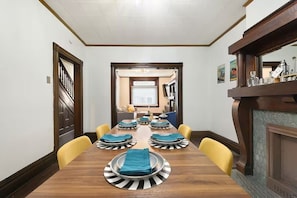 A dining room with a long wooden table set for six, yellow chairs, and a fireplace on the right. - Designer Rowhouse w/ Themed Bedrooms, Fireplace & Arcade — Perfect for Groups (Pittsburgh)