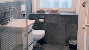 Uma casa de banho moderna com divisória de vidro, sanita, lavatório e janela com vidro jateado.