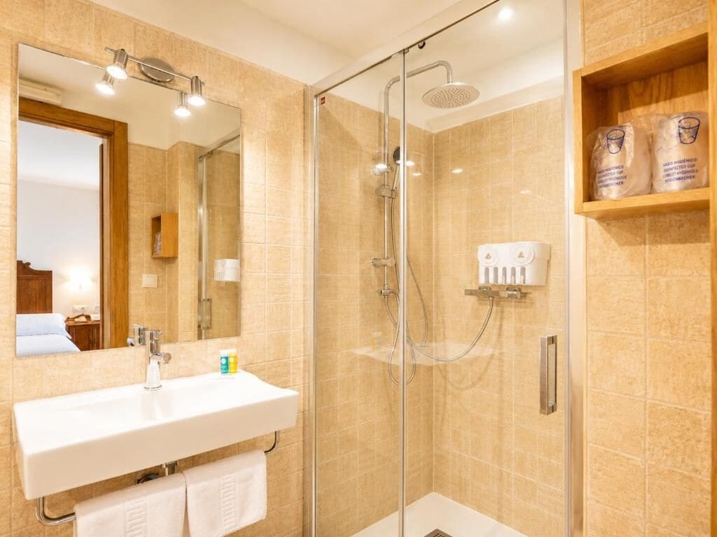 Un baño de hotel con ducha acristalada, lavamanos blanco y espejo.