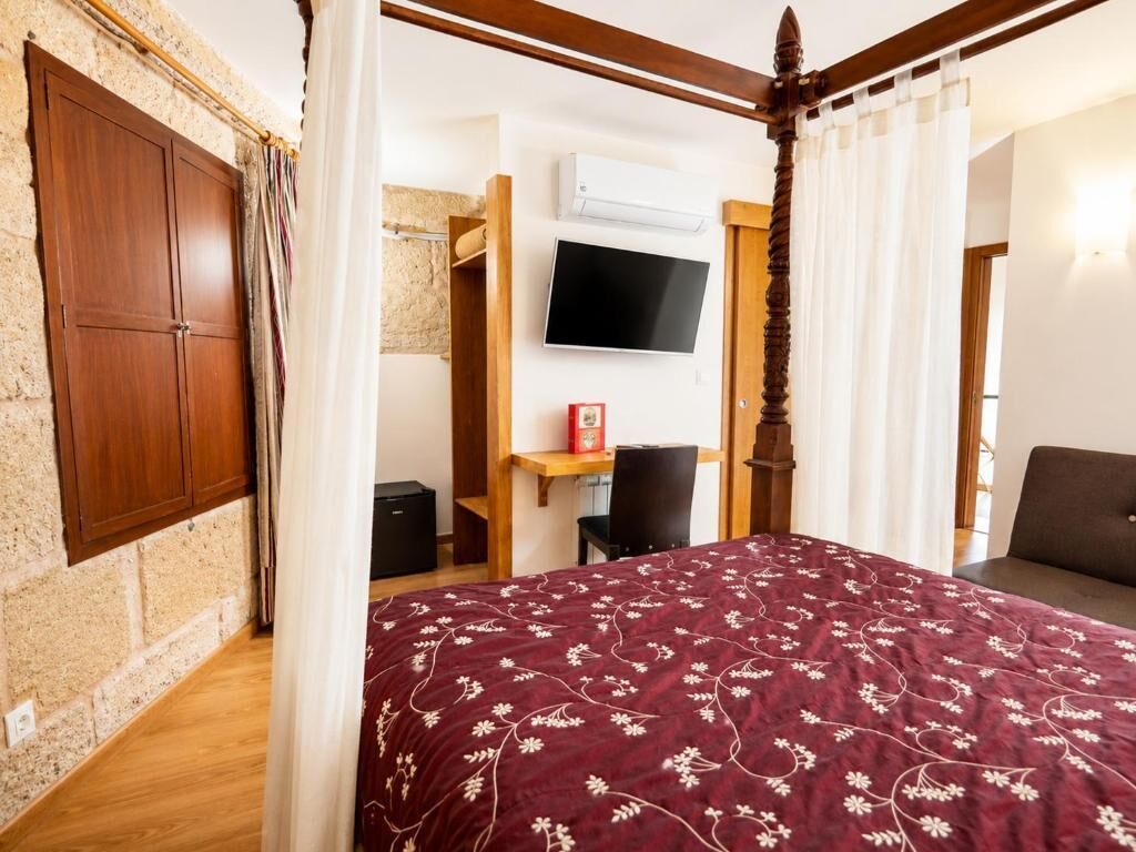 Un dormitorio con una cama con dosel, un escritorio con silla, un televisor y un armario.
