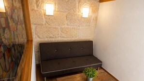 A room with a dark-colored sofa against a stone wall, a small wooden table with a potted plant, and a patterned wall.