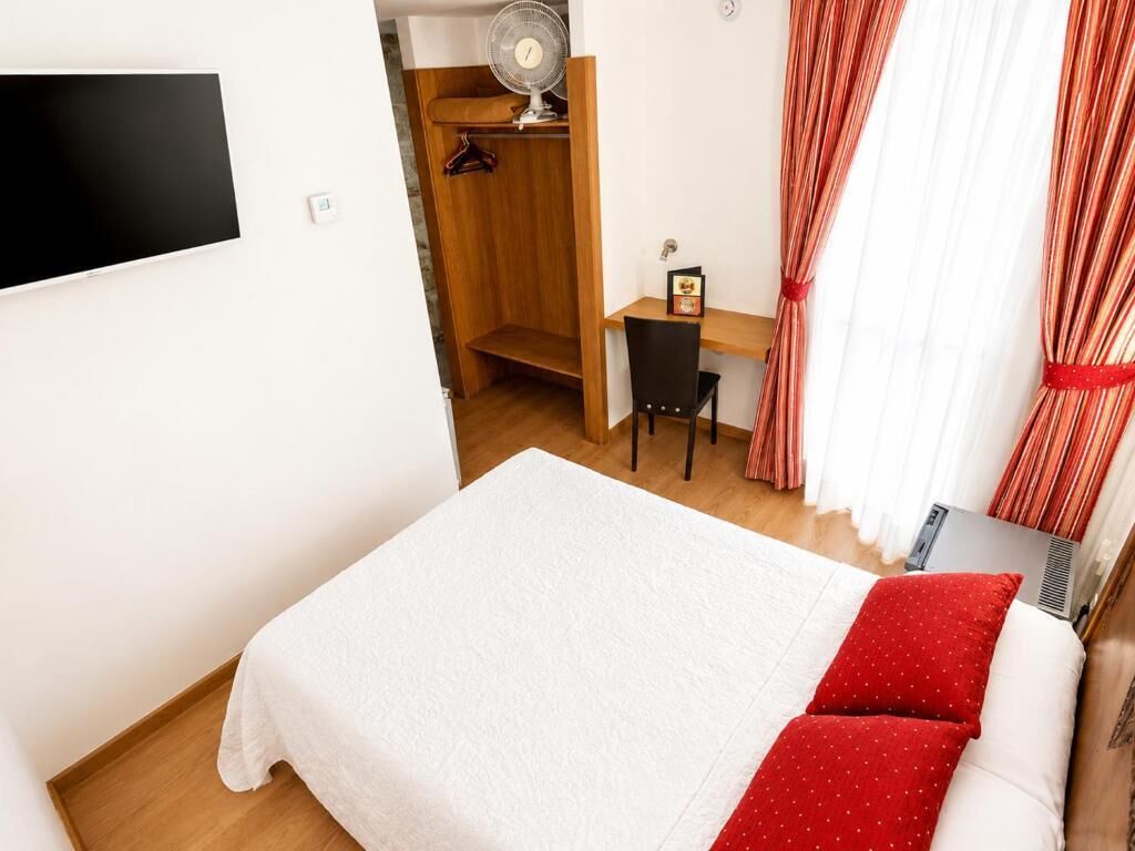 Un dormitorio con cama, escritorio, silla, ventilador y ventana con cortinas.