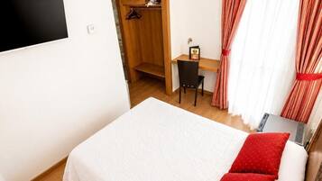 Un dormitorio con cama, escritorio, silla, ventilador y ventana con cortinas.