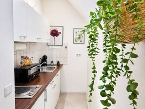 A modern kitchen with white cabinets, a wooden countertop, a coffee machine, and a hanging plant. - Apartment Mutterstadt Oasis One - MIS (Mutterstadt)
