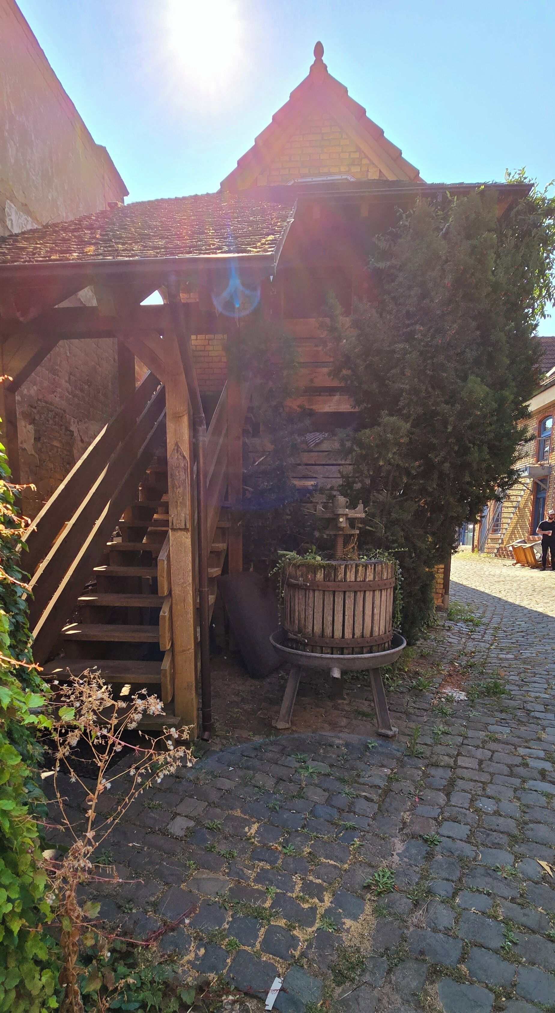 A rustic wooden staircase leading to a covered area with a brick wall and a wooden barrel.