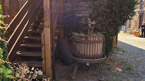 Een houten trap leidt naar een overdekt gedeelte met een bakstenen muur en een houten vat.