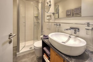 Un baño moderno con ducha envuelta en vidrio, un lavabo blanco y un espejo sobre él.
