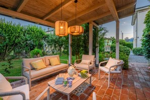 An outdoor seating area with a sofa, chairs, a table, and hanging lights. - Villa Orentano in Orentano (Castelfranco di Sotto)
