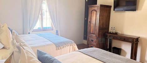 Ein Schlafzimmer mit einem Bett, einem Holzschrank, einem Schreibtisch mit Flachbildfernseher und einem Fenster mit Vorhängen.