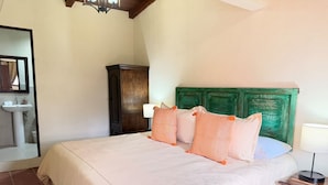 Quarto com cama, mesa de cabeceira, cômoda, espelho e banheiro com pia.