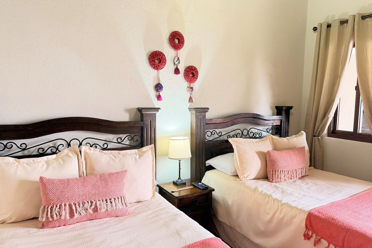 Habitación de hotel con dos camas, una mesita de noche con lámpara y adornos en la pared.