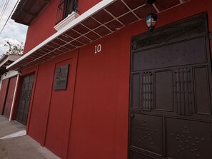 Un edificio rojo con el número '10' grande en la pared, una reja de metal y un letrero con un pájaro y texto.