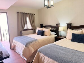 Habitación de hotel con dos camas, una mesita de noche, una lámpara y vistas al exterior.