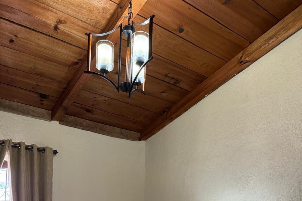 A hotel room with two beds, a wooden ceiling, a window with curtains, and a nightstand with a lamp.
