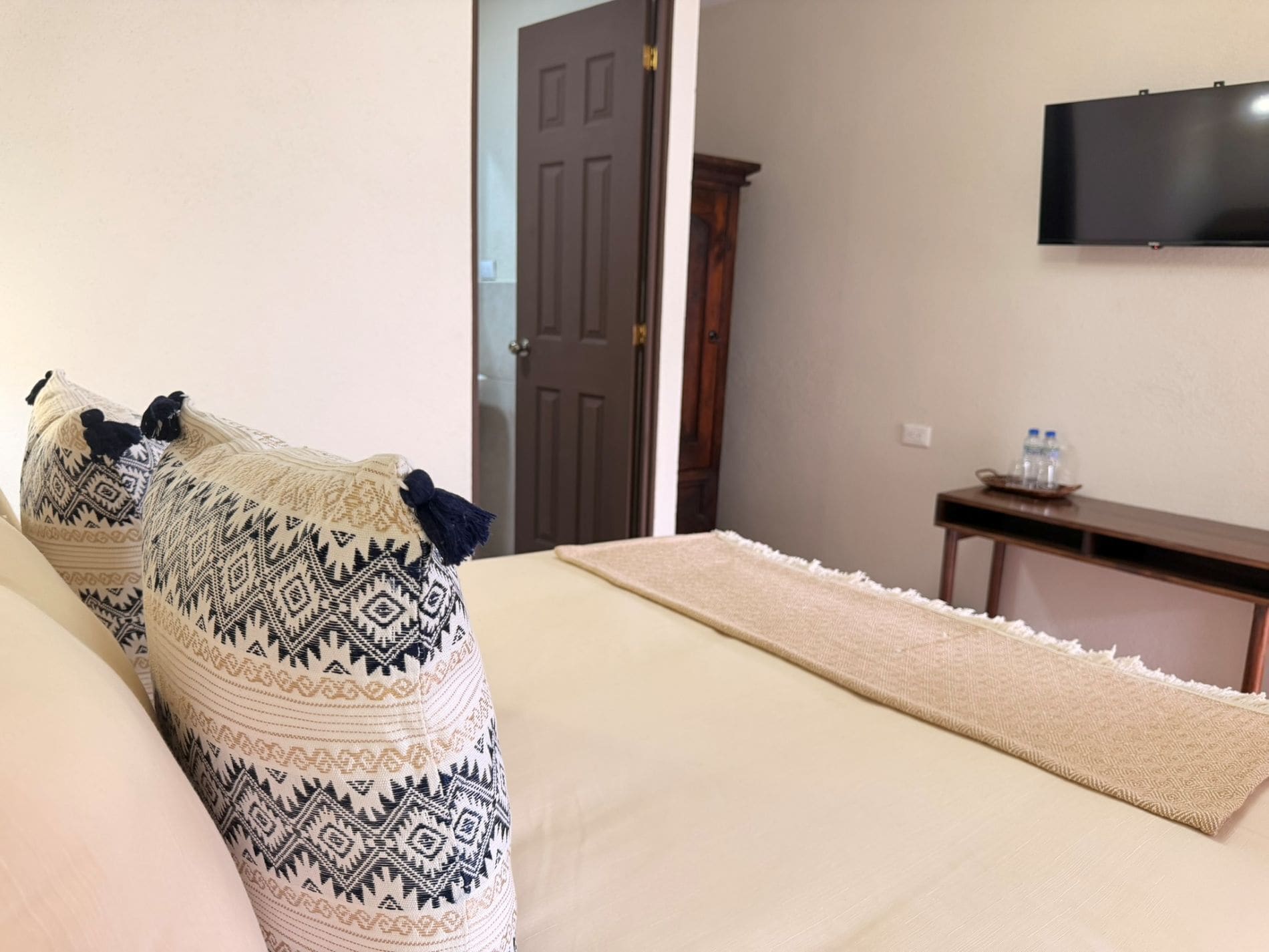 Ein Hotelzimmer mit einem Bett, einem an der Wand befestigten Fernseher, einem Nachttisch aus Holz und einer Tür.