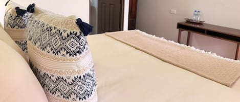 A hotel room with a bed, a television on the wall, a wooden nightstand, and a door.