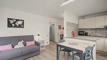 Un apartamento moderno con un sofá gris, una mesa de comedor con sillas, una cocina con armarios blancos y un mapa mundial en la pared.